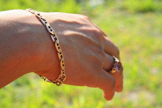 Woman's hand with gold rings and gold bracelet over green grass.