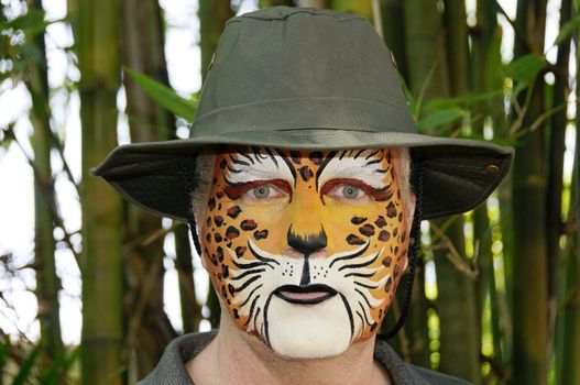 A man with his face painted to look like a leopard wearing a hat.