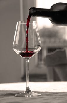 pouring red wine from bottle into wineglass in black and white