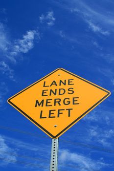 Lane ends road sign over blue sky.
