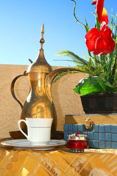 Luxury breakfast set includes brass pitcher and a vase with flowers on a table.