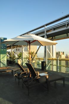 Rooftop lounge chairs under an umbrella face the urban sunset