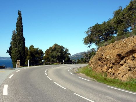 Road in the mountain next to red rocks and trees and vegetation, south France