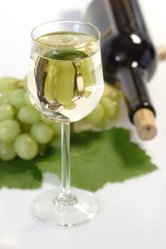 Glass of wine with bottle and grapes on bright background