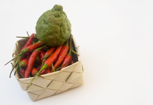 Basket of small chili peppers and a kaffir lime isolated against white, copy space on right
