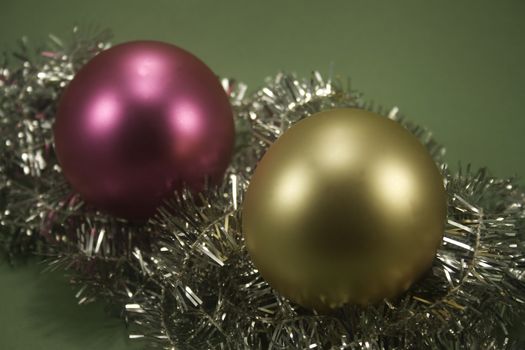 Two ornaments sitting on tinsel and isolated on green paper