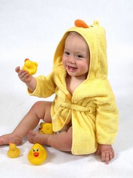 A baby girl in a yellow duck bathrobe holds a plastic toy rubber duck.