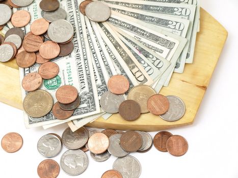 A wooden plate holding US currency fanned out, with coins spilled over it.