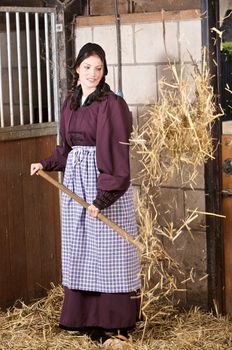 Pretty farmergirl working in the stable throwing new straw in the box