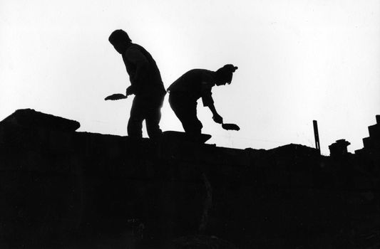 two masons silhouetted as they work on the roof of a building