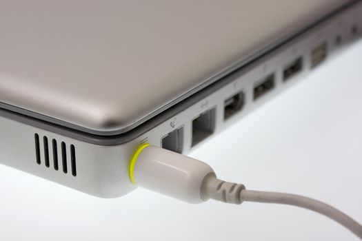 A corner of laptop being charged - focus on a plug with a green light indicating full charge