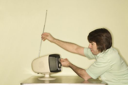 Side view of Caucasian mid-adult man sitting at 50's retro dinette set adjusting old television antenna.