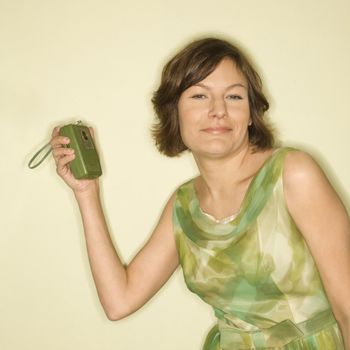 Pretty Caucasian mid-adult woman wearing green vintage dress with handheld radio smiling at viewer.