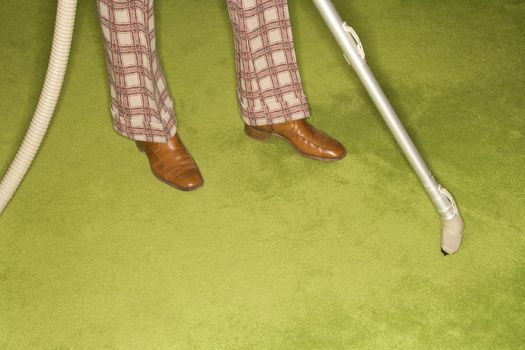 Close-up of Caucasian male feet with vacuum extension against green retro carpet.