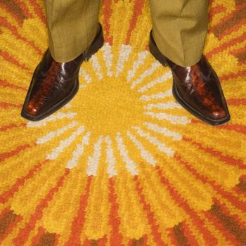 Close-up of Caucasian mid-adult male feet in vintage boots against sunburst rug.