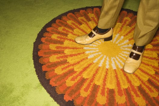Close-up of Caucasian mid-adult male feet in vintage shoes against sunburst rug.