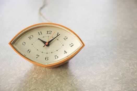 Still life of orange eye-shaped vintage clock on table.