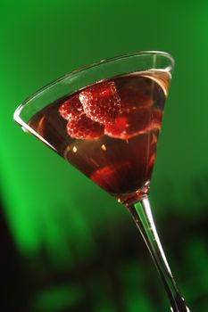 Still life of martini cocktail with raspberries fruit against glowing green background.