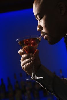 Profile of African American man drinking martini in bar against glowing blue background.