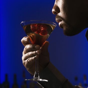 Close up profile of African American man drinking martini in bar against glowing blue background.