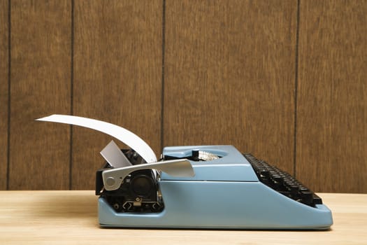 Vintage blue typewriter on desk with wood paneling.