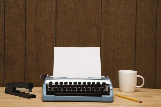 Vintage typewriter, coffee cup, pencil and stapler on desk.