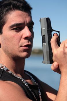 A young man, wearing a sleeveless shirt, holding a hand gun. (This image is part of a series)