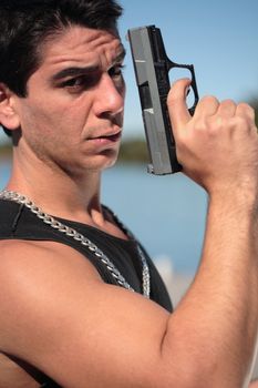 A young man, wearing a sleeveless shirt, holding a hand gun. (This image is part of a series)