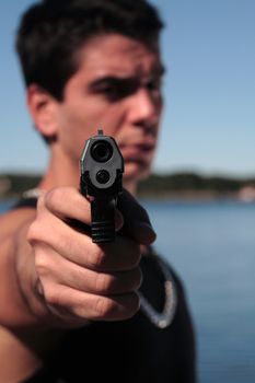 A young man, wearing a sleeveless shirt, holding a hand gun. (This image is part of a series)