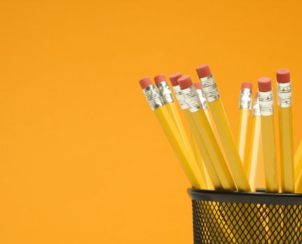 Group of pencils in pencil holder on orange background.