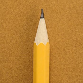 Close up of sharp pencil tip on tan background.