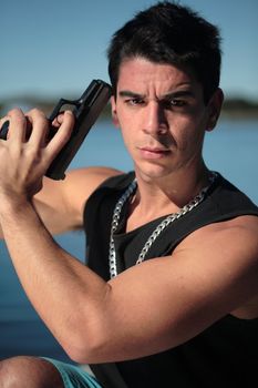 A young man, wearing a sleeveless shirt, holding a hand gun. (This image is part of a series)