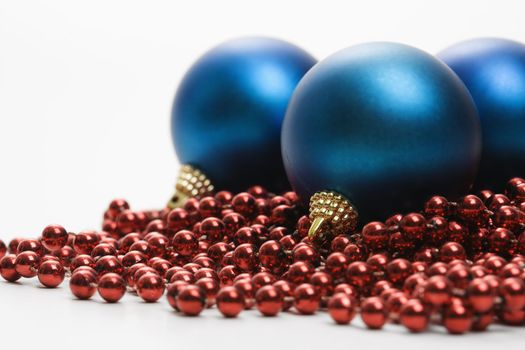 Still life of large blue Christmas ornaments and strings of red beads.