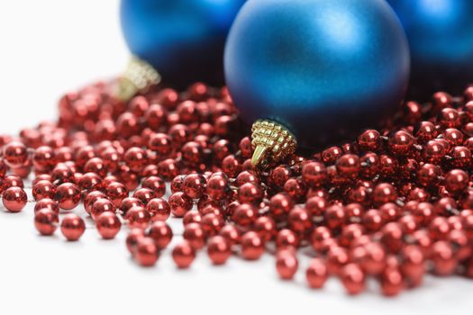 Still life of large blue Christmas ornaments and strings of red beads.