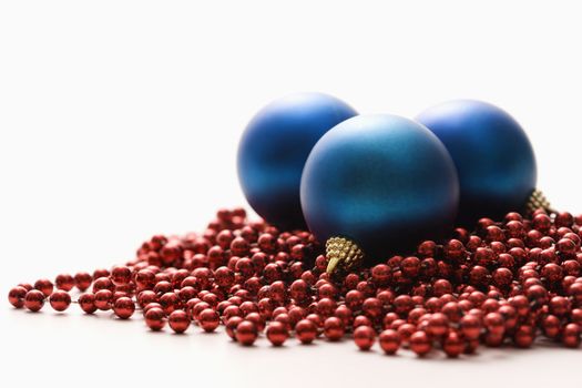 Still life of large blue Christmas ornaments and strings of red beads.