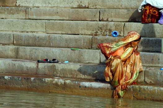 Woman in yellow sari seat on steps by rivers edge. Varanasi Uttar Pradesh India