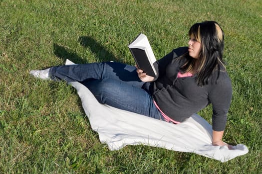 A young woman with highlighted hair reading a book or doing homework on campus.