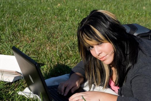 A young student using her laptop computer while laying in the grass on a nice day.