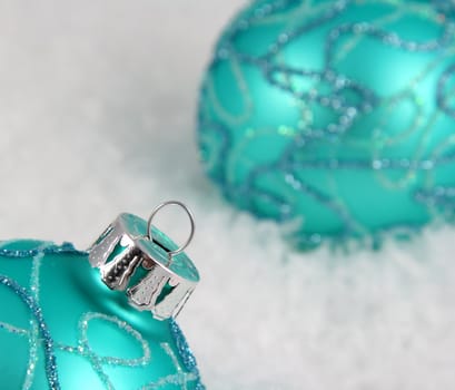 Two aqua Christmas baubles sitting in the snow.