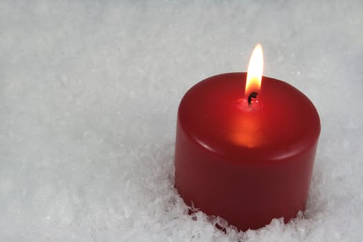 A red lit candle sitting in a bed of snow.