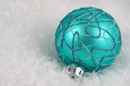 An aqua Christmas bauble sitting in a bed of snow.
