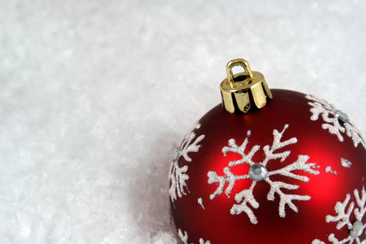 A snowflake Christmas bauble sitting in a bed of snow.
