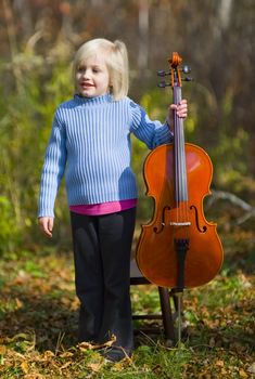 A child standing with her cello outside on a crisp autumn day.
