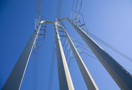 White power pole tower with lots of power lines from its base to the blue sky
