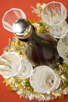 Five glasses with wine bottle and Christmas decoration on red background.