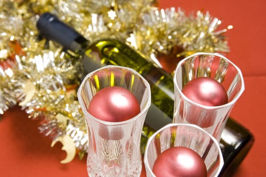 Three glasses with wine bottle and Christmas decoration on red background.