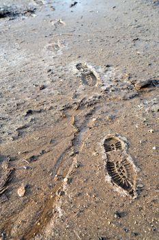 Boot prints crossing partially frozen mud and ice