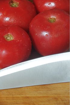 ripe fresh tomatoes with knife over a wood cutting board