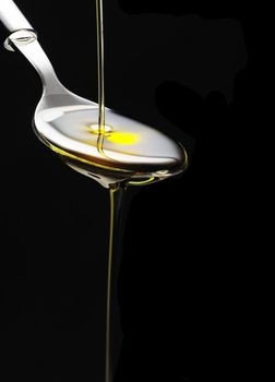 olive oil poured on a spoon over black background