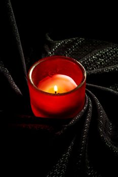 candle on a red glass holder over a black fabric background